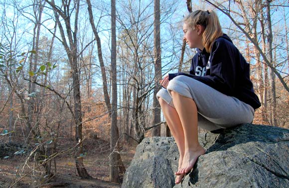 A young woman sitting on a stone looking into the wood.